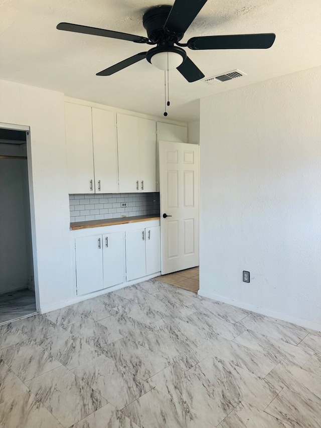 interior space with marble finish floor, tasteful backsplash, visible vents, wooden counters, and white cabinets