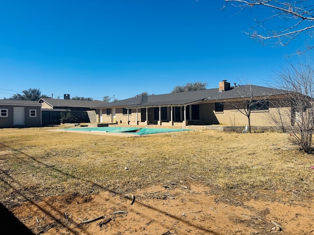 rear view of property with an outdoor structure, a lawn, a fenced in pool, a chimney, and a patio area