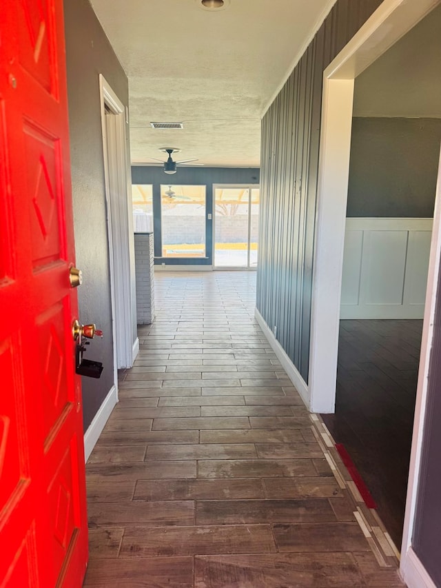 hall with visible vents, a decorative wall, wood finished floors, and wainscoting