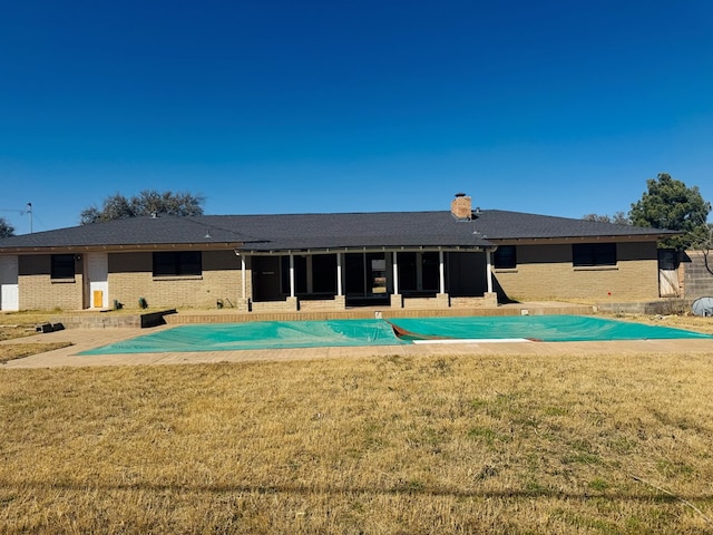 rear view of property with a yard, brick siding, a chimney, and a sunroom