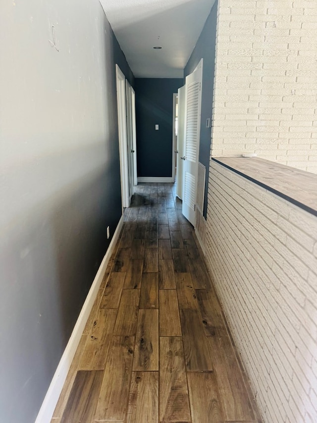 corridor featuring dark wood-style floors, brick wall, and baseboards