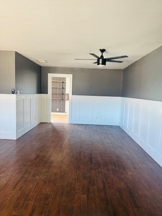 unfurnished room with visible vents, a wainscoted wall, ceiling fan, wood finished floors, and a decorative wall