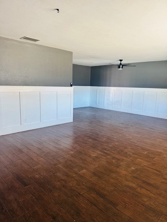 empty room with dark wood-style floors, wainscoting, visible vents, and a decorative wall