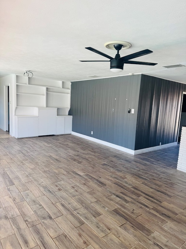 unfurnished living room with visible vents, ceiling fan, a textured ceiling, wood finished floors, and baseboards