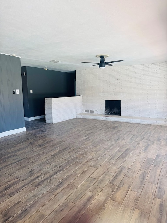 unfurnished living room with visible vents, a brick fireplace, wood finished floors, and a ceiling fan