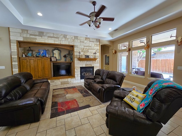 tiled living room with a ceiling fan, a stone fireplace, visible vents, a raised ceiling, and recessed lighting