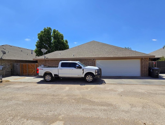 view of side of property with a garage, fence, roof with shingles, brick siding, and driveway