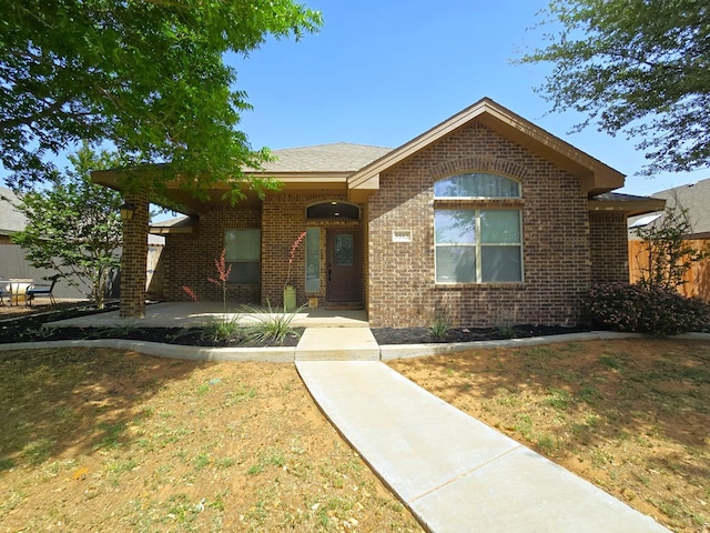 view of front of property featuring brick siding, fence, and a patio