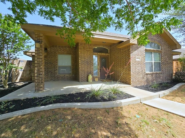view of front of property featuring brick siding, fence, and a patio