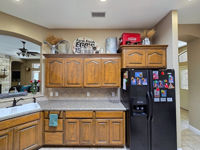 kitchen featuring arched walkways, black fridge, brown cabinets, and visible vents
