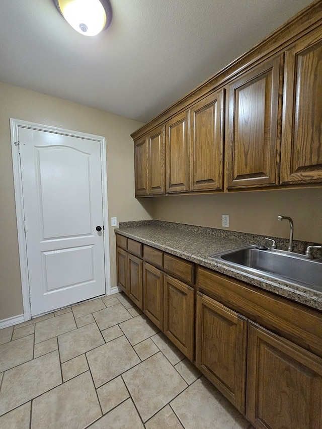 laundry room featuring baseboards, a sink, and light tile patterned floors