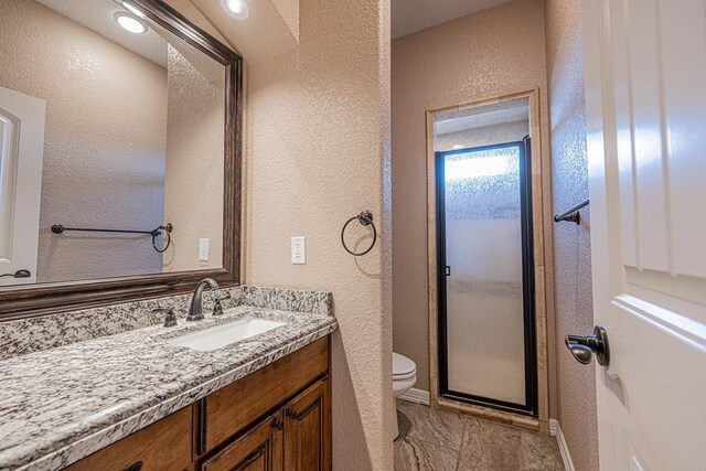 2894 SE 5001, Andrews, TX 79714 - bathroom with toilet, a textured wall, vanity, baseboards, and a shower with door