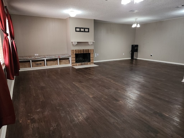 unfurnished living room featuring a chandelier, a textured ceiling, dark hardwood / wood-style flooring, and a brick fireplace