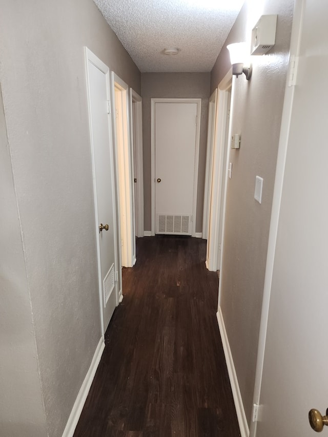 corridor featuring a textured ceiling and dark hardwood / wood-style flooring