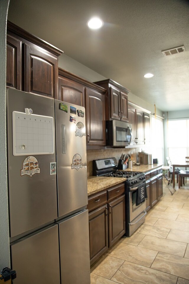 kitchen with light stone countertops, dark brown cabinetry, and appliances with stainless steel finishes