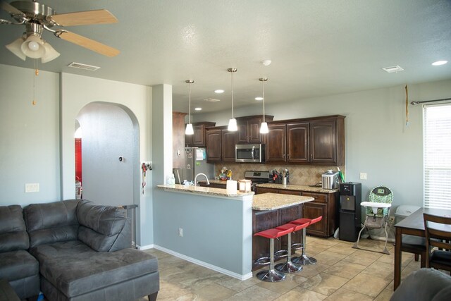 kitchen with kitchen peninsula, appliances with stainless steel finishes, a kitchen breakfast bar, dark brown cabinetry, and decorative light fixtures