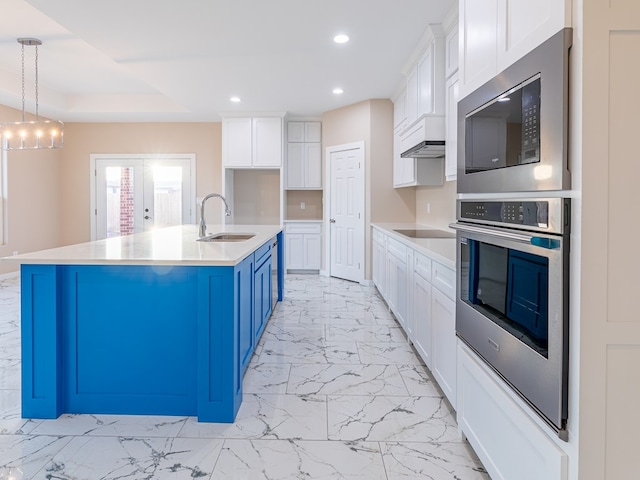 kitchen with sink, hanging light fixtures, stainless steel oven, a center island with sink, and blue cabinets