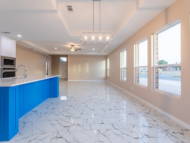 kitchen featuring decorative light fixtures, a raised ceiling, stainless steel oven, ceiling fan, and built in microwave