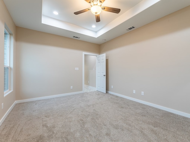 empty room featuring ceiling fan, light colored carpet, and a tray ceiling