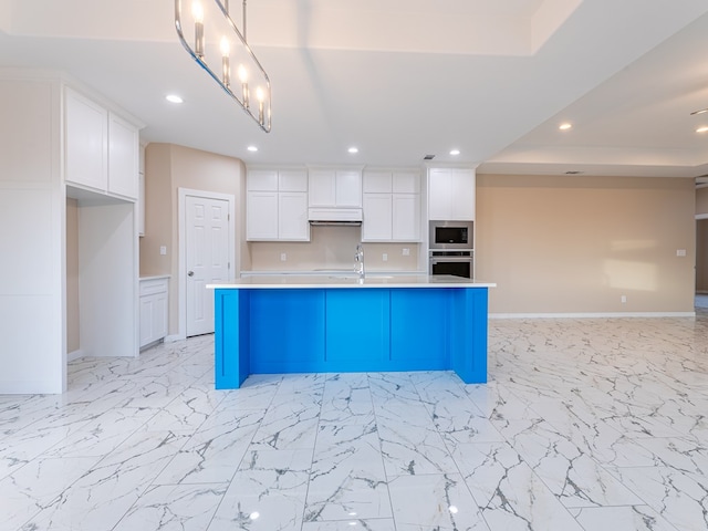 kitchen featuring a kitchen breakfast bar, appliances with stainless steel finishes, white cabinets, and a center island with sink