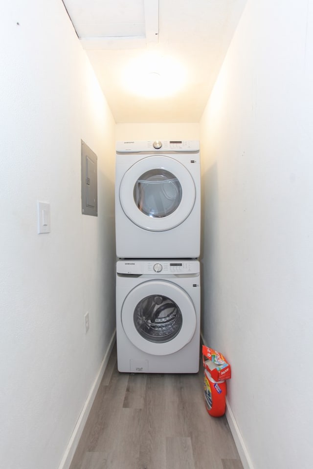 laundry room with electric panel, stacked washer and dryer, and wood-type flooring