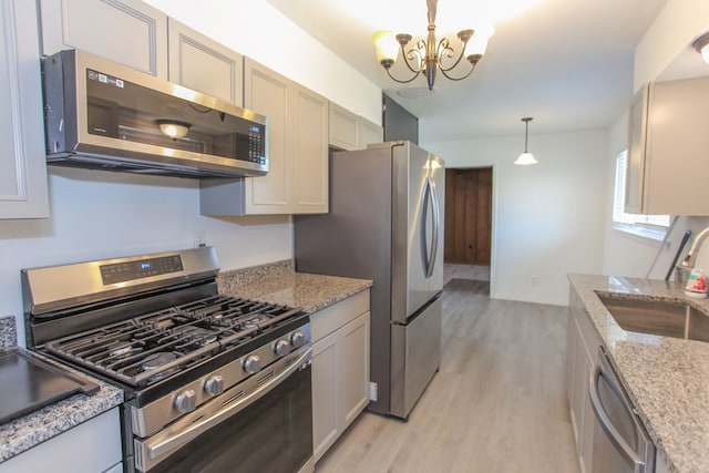 kitchen featuring light stone counters, stainless steel appliances, sink, decorative light fixtures, and a chandelier