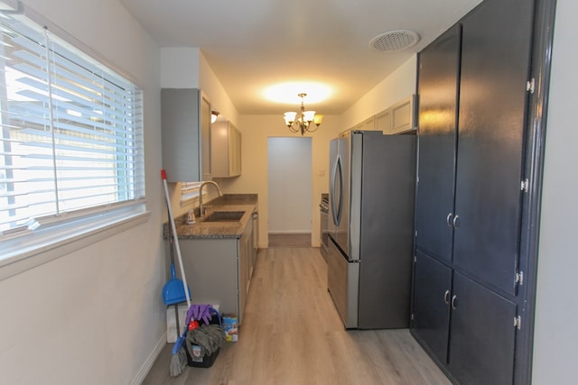 kitchen featuring pendant lighting, sink, light hardwood / wood-style floors, stainless steel refrigerator, and a chandelier