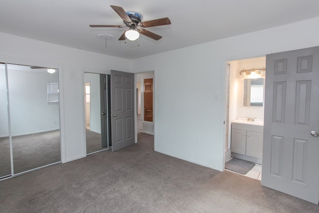 unfurnished bedroom with ceiling fan, multiple closets, light carpet, and ensuite bath