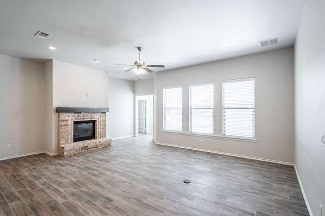 unfurnished living room featuring a brick fireplace, ceiling fan, visible vents, and wood finished floors