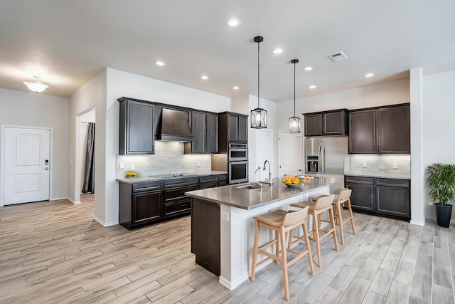 kitchen with a breakfast bar area, stainless steel appliances, a sink, visible vents, and custom exhaust hood