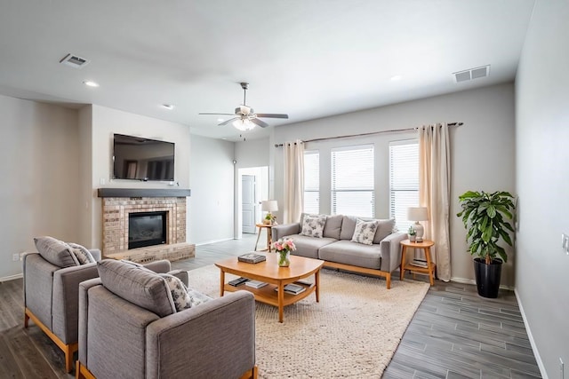 living room with wood finished floors, a ceiling fan, visible vents, baseboards, and a brick fireplace