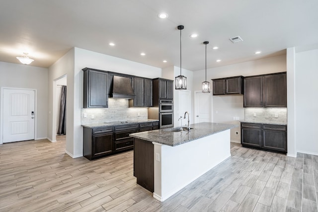 kitchen with stone counters, stainless steel double oven, a sink, premium range hood, and black electric cooktop