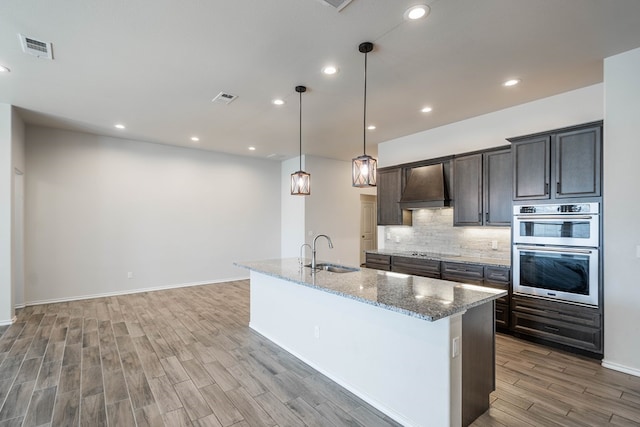 kitchen with visible vents, a sink, custom exhaust hood, black electric cooktop, and backsplash