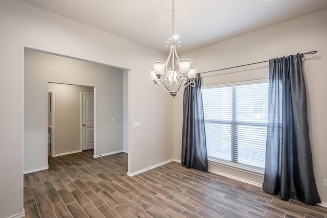 empty room with lofted ceiling, an inviting chandelier, wood tiled floor, and baseboards