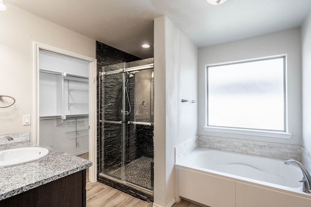 full bathroom featuring a spacious closet, vanity, a shower stall, wood finished floors, and a bath