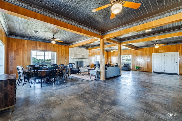 dining space featuring beamed ceiling, wood walls, and a stone fireplace