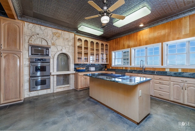 kitchen with light brown cabinets, stainless steel appliances, dark stone countertops, wood walls, and a kitchen island