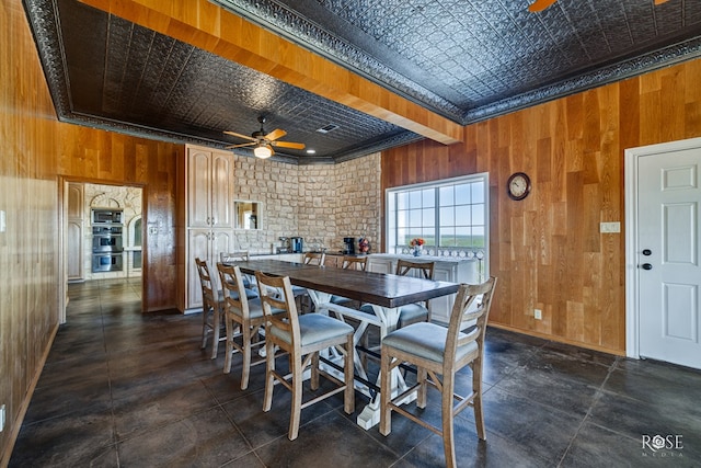 dining space with ceiling fan, crown molding, and wood walls