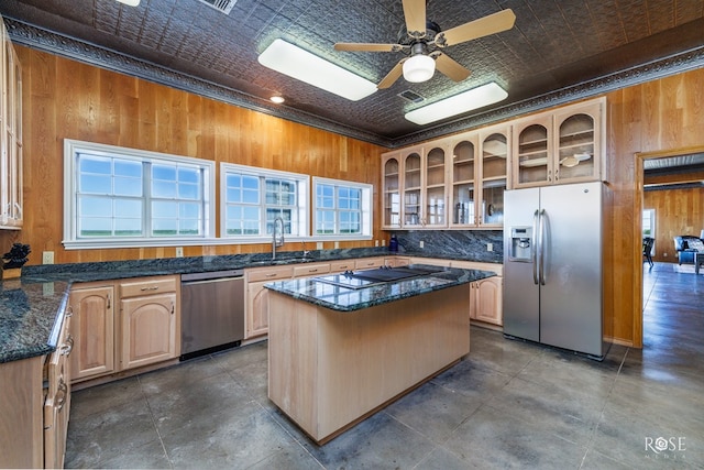 kitchen featuring appliances with stainless steel finishes, dark stone counters, ceiling fan, wooden walls, and a kitchen island