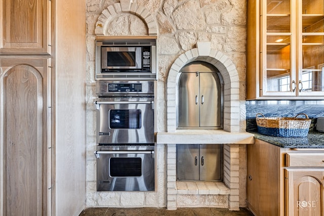 kitchen featuring light brown cabinetry, backsplash, appliances with stainless steel finishes, and dark stone counters