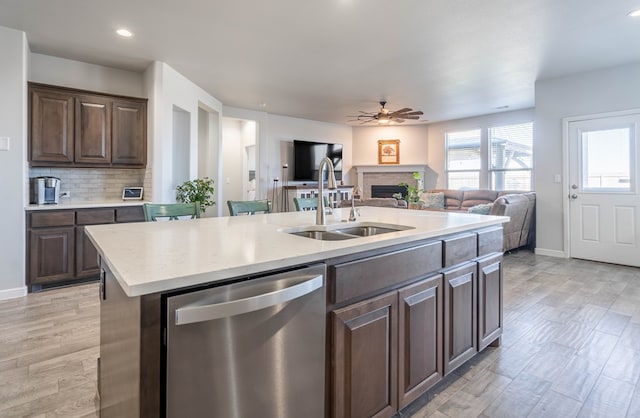 kitchen featuring a center island with sink, sink, stainless steel dishwasher, ceiling fan, and dark brown cabinetry