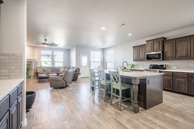 kitchen with stainless steel appliances, tasteful backsplash, light hardwood / wood-style flooring, a breakfast bar area, and a center island with sink