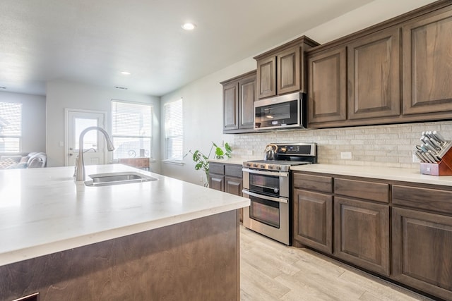 kitchen with sink, tasteful backsplash, light hardwood / wood-style floors, dark brown cabinets, and appliances with stainless steel finishes