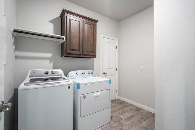 clothes washing area with washer and dryer, light hardwood / wood-style flooring, and cabinets