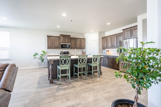 kitchen featuring backsplash, a kitchen bar, a center island with sink, appliances with stainless steel finishes, and light wood-type flooring