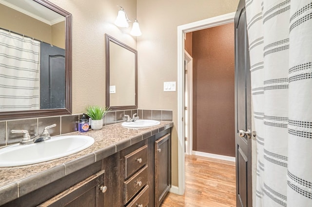 bathroom with vanity, wood-type flooring, ornamental molding, and tasteful backsplash