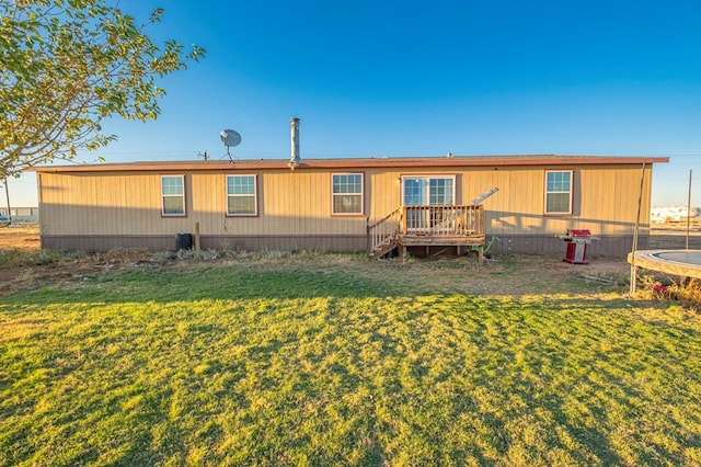 back of house featuring a deck, a trampoline, and a yard