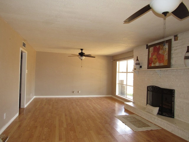 unfurnished living room with visible vents, baseboards, a brick fireplace, ceiling fan, and light wood-style flooring