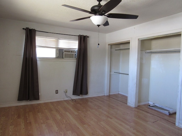unfurnished bedroom featuring baseboards, two closets, ceiling fan, a textured ceiling, and wood finished floors