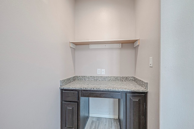 bar with dark brown cabinetry, light stone counters, and light hardwood / wood-style floors